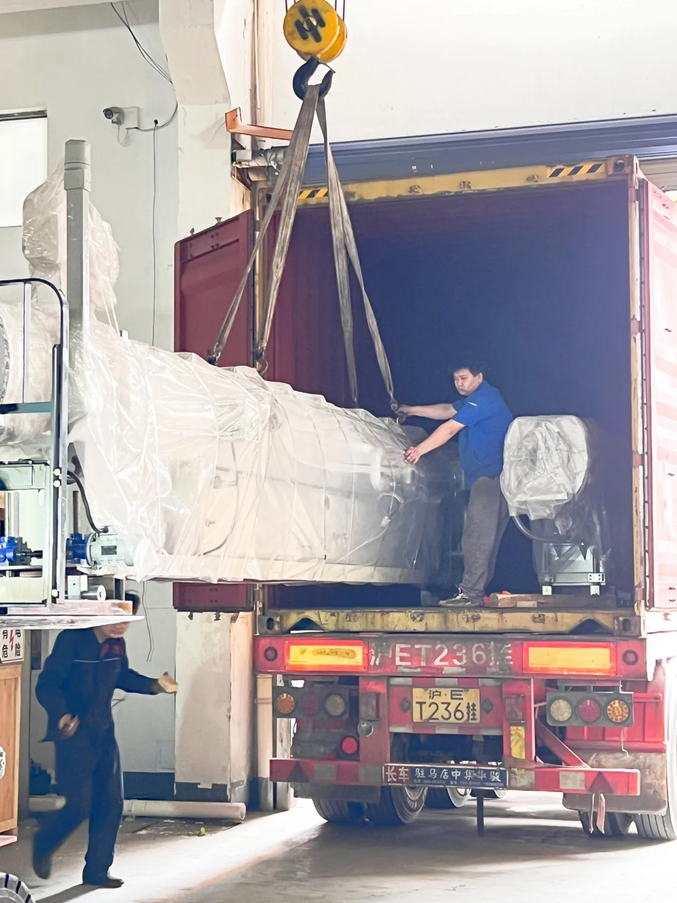 Workers guiding wrapped machinery into the container